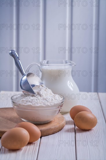 Eggs flour in transparent bowl jug with milk on white lacquered old wooden board Eating and drinking concept