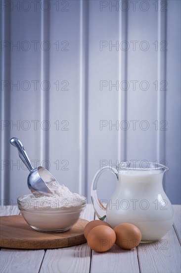 Jug with milk bowl Flour Egg on white lacquered wooden board Food and drink Still life