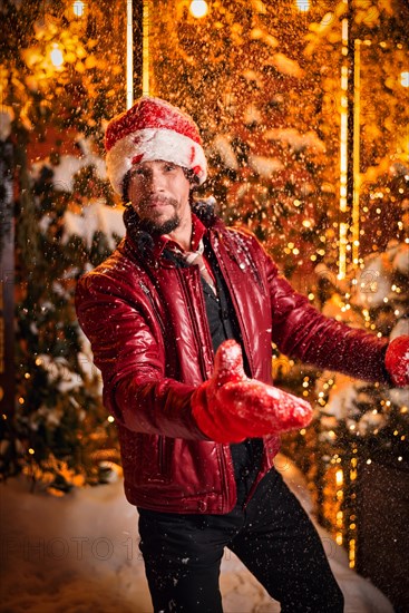 Man dressed as Santa Claus throws up snow on a street decorated with garlands. New Year and Christmas concept. Mixed media