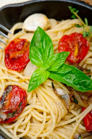 Italian spaghetti pasta with baked tomatoes basil and thyme sauce on a cast iron skillet