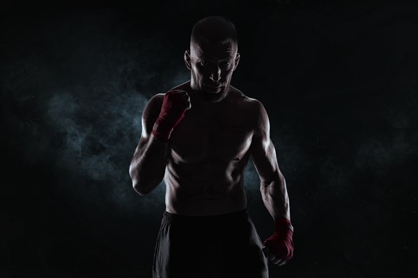 Kickboxer in red bandages poses against a background of smoke. The concept of mixed martial arts. MMA