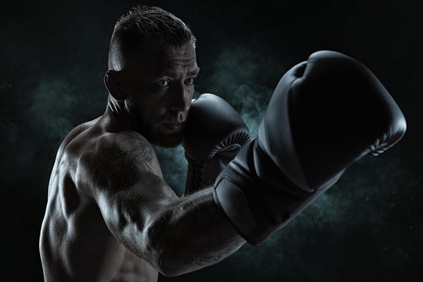 Kickboxer in black gloves posing on a background of smoke. The concept of mixed martial arts. MMA