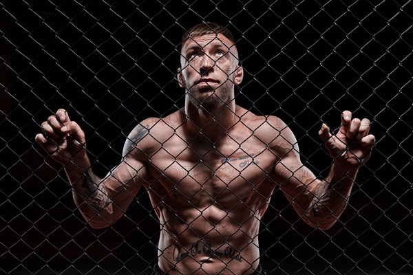 Dramatic image of a mixed martial arts fighter standing in an octagon cage. Powerful abdominal muscles. The concept of sports