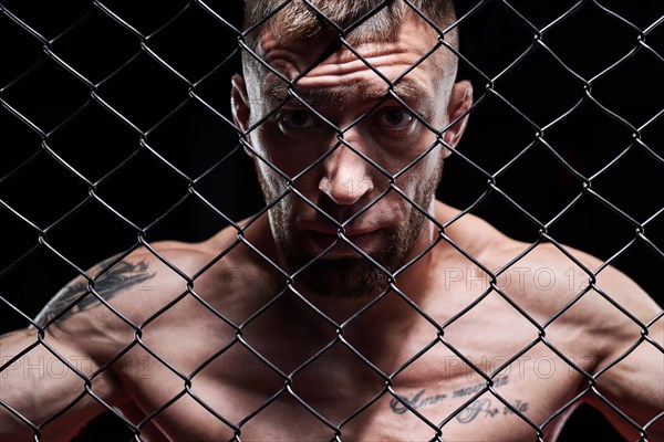 Portrait of a powerful fighter behind the steel bars of the octagon. The concept of sports