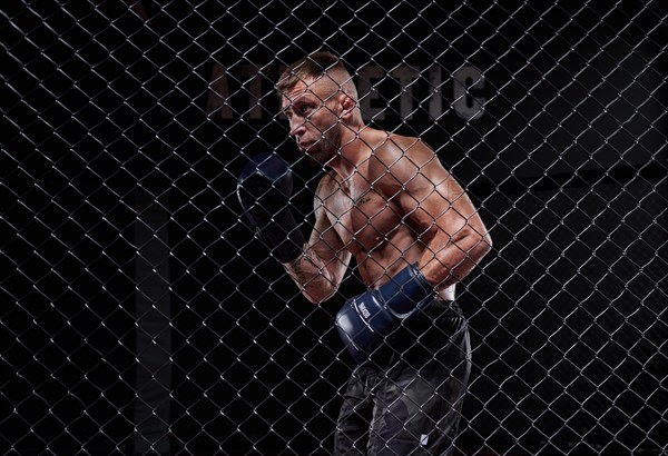 Dramatic image of a mixed martial arts fighter standing in an octagon cage. The concept of sports