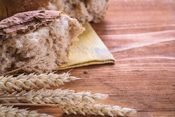 Slice of bread with ears of wheat on an old wooden board horizontal version