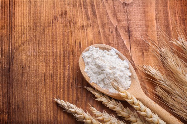 Flour in wooden spoon with ears of wheat on wooden table with copy space