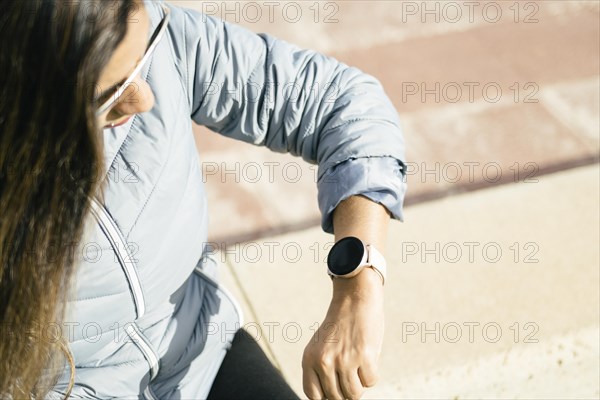 Latin woman with long hair looking at smartwatch wearing sunglasses and blue jacket