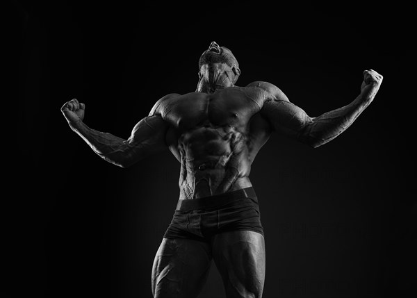 Silhouette of a strong bodybuilder. Confident young fitness athlete with a powerful body and perfect abs. Black and white photography. Dramatic light. Mixed media