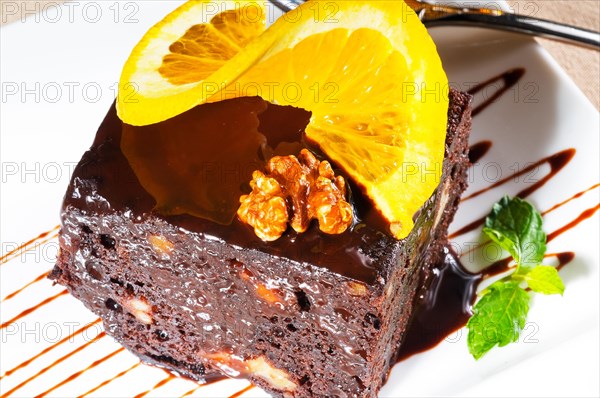 Fresh baked delicious chocolate and walnuts cake with slice of orance on top and mint leaf