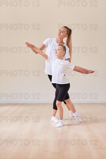 Beautiful woman teacher and a little girl perform dance movements in a bright studio. The concept of education