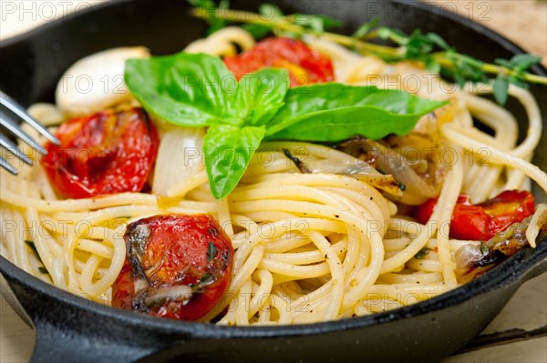 Italian spaghetti pasta with baked tomatoes basil and thyme sauce on a cast iron skillet