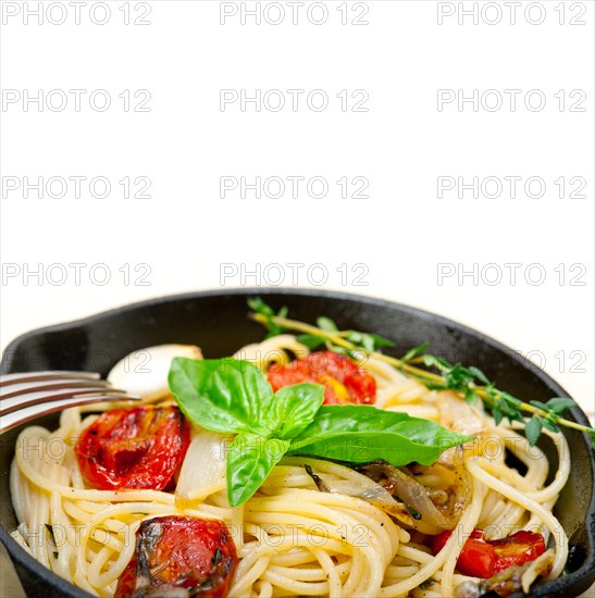 Italian spaghetti pasta with baked tomatoes basil and thyme sauce on a cast iron skillet