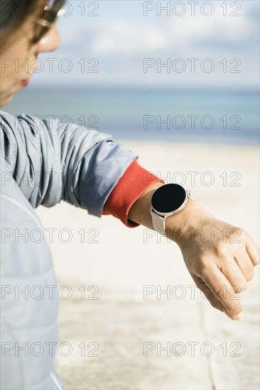 Cropped photo of a stylish woman checks notification on wearable digital wrist watch monitors the weather wears casual jacket poses on the street. Woman uses modern gadget on the street