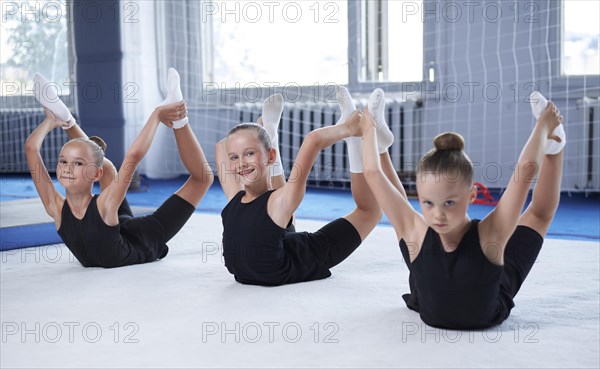 A group of three little girls train on a white mat in a sports club. Gymnastics concept. Mixed media