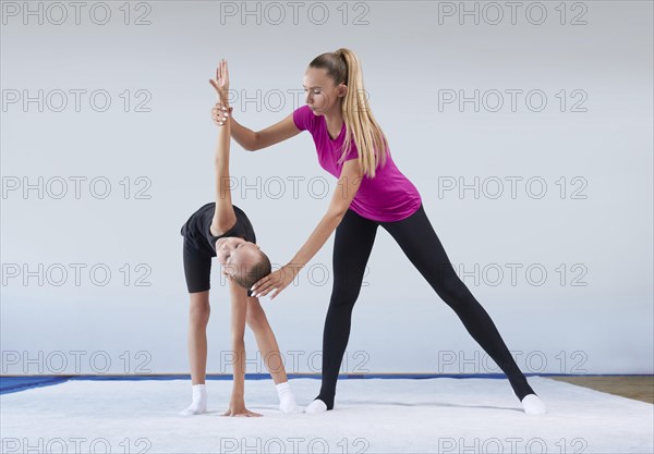 Training in the gym class. A little girl under the guidance of a trainer performs exercises. Gymnastics concept. Mixed media