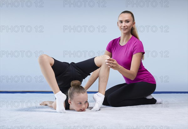 Training in the gym class. A little girl under the guidance of a trainer performs exercises. Gymnastics concept. Mixed media