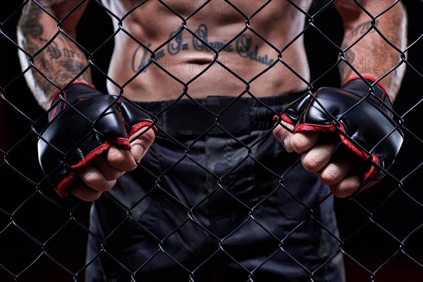 Dramatic image of a mixed martial arts fighter standing in an octagon cage. Powerful abdominal muscles. The concept of sports