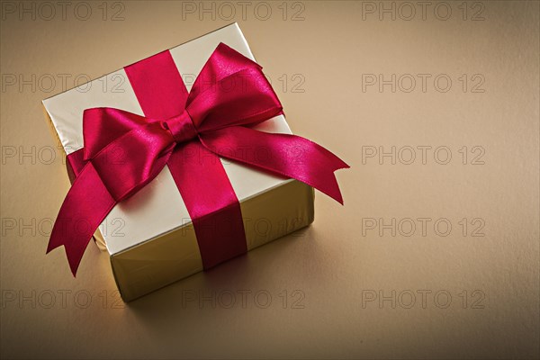 Boxed present with tied bow on golden background holidays concept