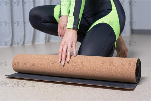Image of a young woman in a gymnastics suit rolling up a mat after a workout. The concept of fitness