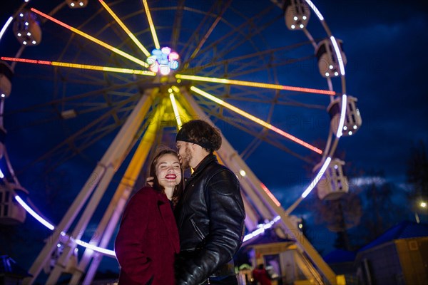 Couple in love in an amusement park near a ferris wheel on a date in cold weather. The concept of love and joy in relationships