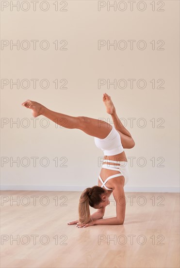 Flexible woman in white sportswear took a bridge position on her hands and gracefully spread her legs. The concept of gymnastics