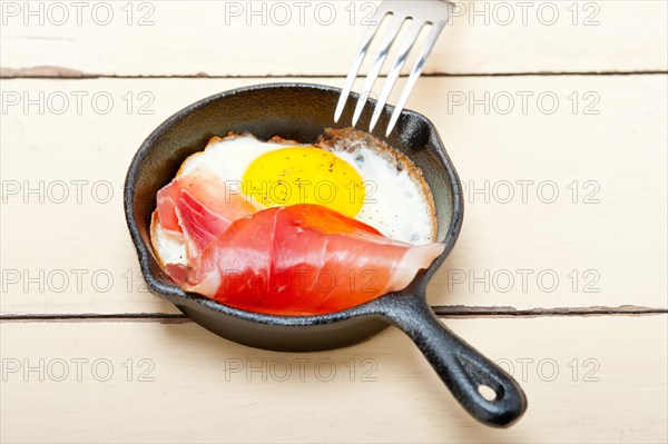 Fried egg sunny side up with Italian tyrolean speck smoked ham on a skillet