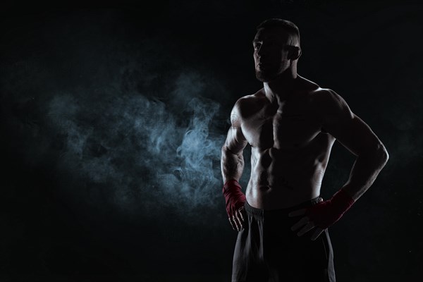 Kickboxer in red bandages poses against a background of smoke. The concept of mixed martial arts. MMA