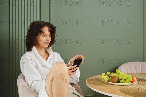 Young woman dialing her friend's number while sitting at table after shower