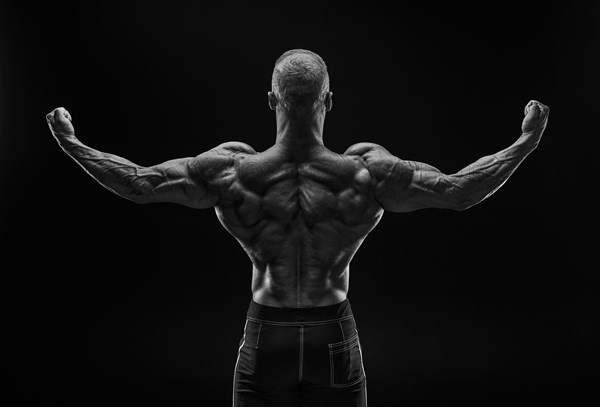 Silhouette of a strong bodybuilder. View from the back. Confident young fitness athlete with a powerful body and perfect abs. Black and white photography. Dramatic light