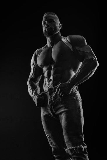 Silhouette of a strong bodybuilder. Confident young fitness athlete with a powerful body and perfect abs. Black and white photography. Dramatic light. Mixed media