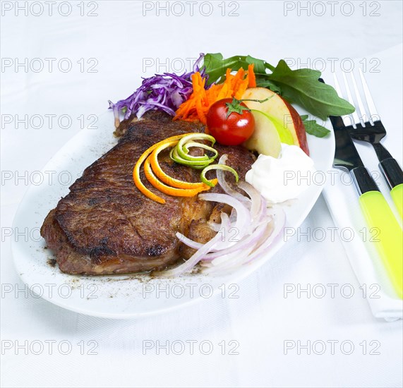 Fresh juicy beef ribeye steak grilled with lemon and orange peel on top and vegetables beside with sour cream