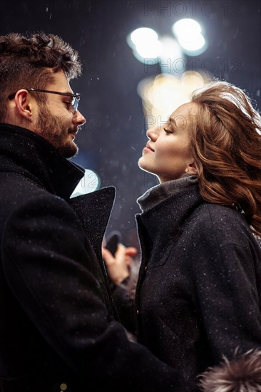 Young beautiful couple in love dancing in the city under snowfall on valentine's day