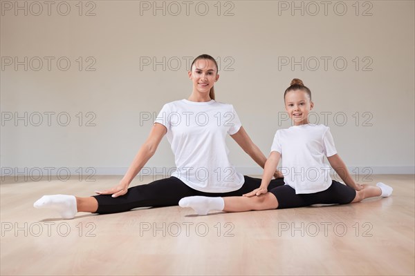 Beautiful female teacher and a little girl are sitting in the splits in a gymnastics class. The concept of education