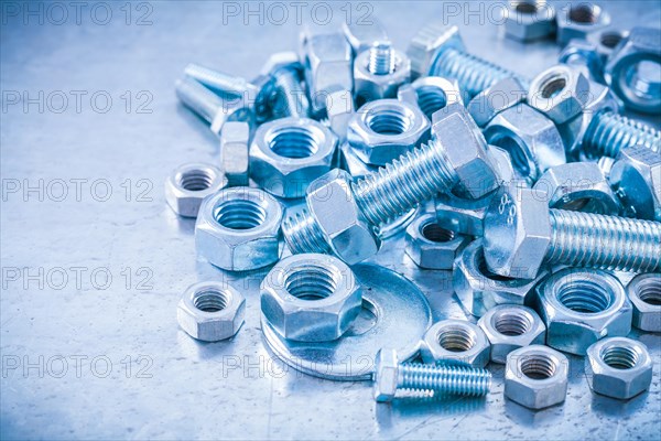 Big stack of metal threaded screwbolts nuts and bolt washers on metallic background construction concept