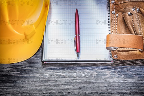 Leather construction belt building helmet copybook pen on wooden board directly above