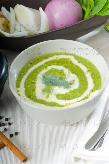 Fresh spinach soup on a white bowl with sage and cream on top