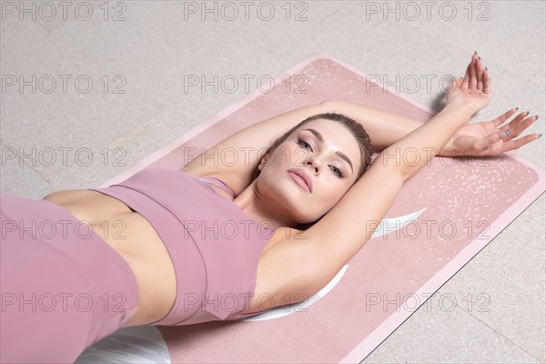 Beauty portrait of a charming woman in a gymnastic suit lying on a mat in a bright studio. The concept of fitness
