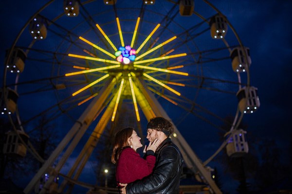 Couple in love in an amusement park near a ferris wheel on a date in cold weather. The concept of love and joy in relationships