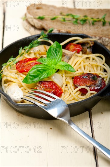 Italian spaghetti pasta with baked tomatoes basil and thyme sauce on a cast iron skillet