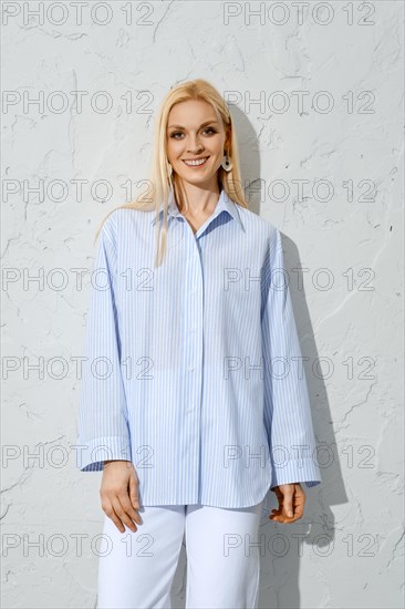 Comfortable summer outfit. Smiling woman in blue cotton blouse next to white wall