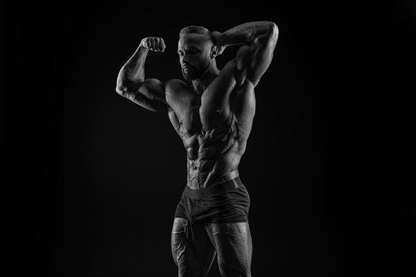 Silhouette of a strong bodybuilder. Confident young fitness athlete with a powerful body and perfect abs. Black and white photography. Dramatic light. Mixed media