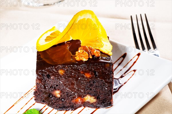 Fresh baked delicious chocolate and walnuts cake with slice of orance on top and mint leaf