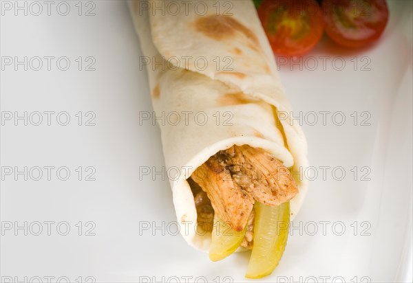 Pita bread chicken roll with pickles cucumbers on a plate with pachino tomatoes and lettuce