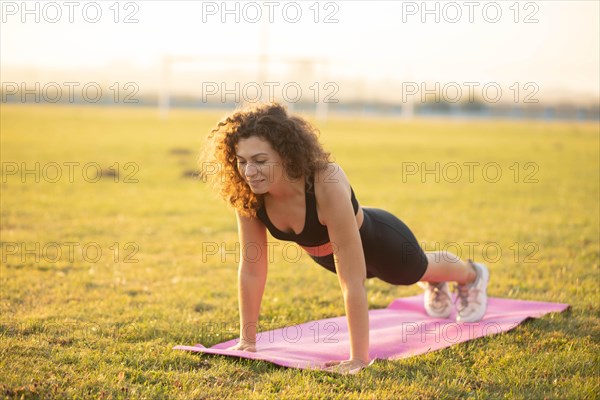 Curly girl runner doing plank exercise on a yoga mat on the lawn