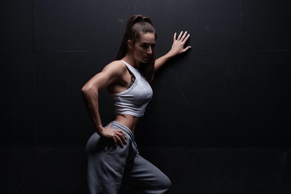 Athletic fitness woman posing in the studio on a dark background. Photo of an attractive woman in fashionable sportswear. Sports and healthy lifestyle. Mixed media
