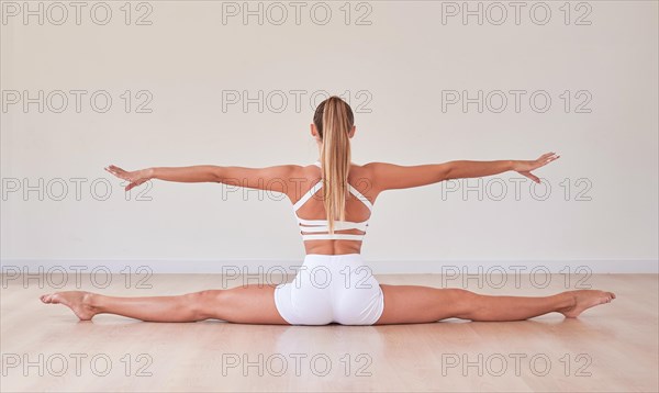 Flexible woman in white sportswear took a splits-legs pose. The concept of gymnastics