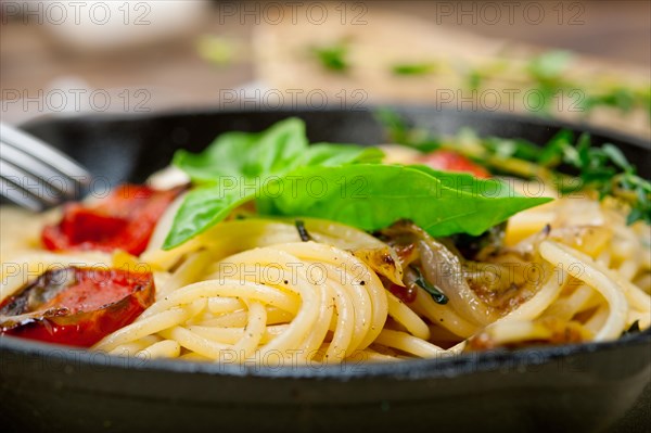 Italian spaghetti pasta with baked tomatoes basil and thyme sauce on a cast iron skillet