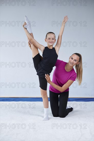 Training in the gym class. A little girl under the guidance of a trainer performs exercises. Gymnastics concept. Mixed media