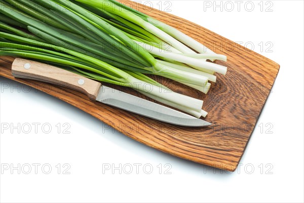Green spring onion scallion stems with kitchen knife on wooden cutting board isolated white